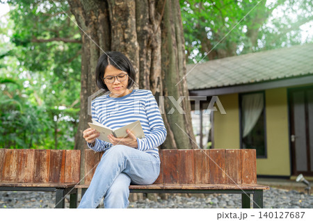 Asian mature woman reading a book on wooden bench in a peaceful garden. Nature, self-care, and quiet reflection. Mindful slow living lifestyle. Personal growth, emotional healing. mindful life balance Asian mature woman reading a book on wooden bench in a peaceful garden. Nature, self-care, and quiet reflection. Mindful slow living lifestyle. Personal growth, emotional healing. mindful life balance 140127687