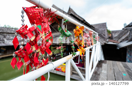Brightly colored paper decorations hanging from a white railing at a traditional wooden house near the water, creating a vibrant cultural scene ideal for festival and travel photography. 140127799