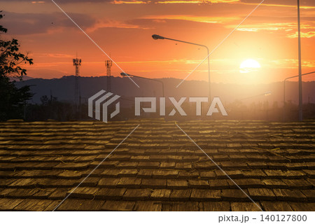 Wooden roof tiles glowing under warm sunlight during sunset with communication towers and hills in background. Natural texture, architectural detail, and peaceful countryside evening atmosphere. Wooden roof tiles glowing under warm sunlight during sunset with communication towers and hills in background. Natural texture, architectural detail, and peaceful countryside evening atmosphere. 140127800
