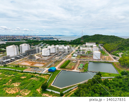 Gas storage tanks in lush green hill and forest. Industrial petrochemical facility with extensive steel pipeline network and water reservoir. Energy infrastructure balancing with natural environment. Gas storage tanks in lush green hill and forest. Industrial petrochemical facility with extensive steel pipeline network and water reservoir. Energy infrastructure balancing with natural environment. 140127831
