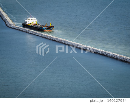 Marine construction vessel working on stone breakwater project in ocean. Coastal infrastructure development and harbor protection engineering work in progress. Port construction and coastal defense. 140127954