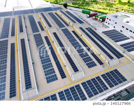 Solar-powered warehouse facility with freight trucks at loading docks. Eco-friendly logistics and efficient cargo transportation. Solar panels and sustainable energy concept in distribution center. 140127966