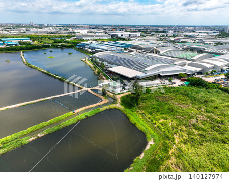 A modern industrial factory complex with solar panels installed on warehouse rooftops beside wastewater treatment ponds. Sustainable energy integration and eco-friendly production management. A modern industrial factory complex with solar panels installed on warehouse rooftops beside wastewater treatment ponds. Sustainable energy integration and eco-friendly production management. 140127974