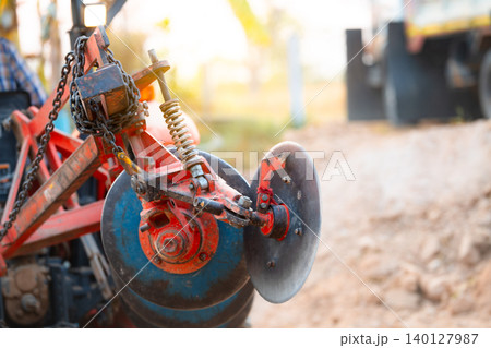 Close-up of modern disc harrow attachment on agricultural tractor in rural countryside. Essential farm machinery for soil preparation, improving field conditions, and enhancing crop growth efficiency. Close-up of modern disc harrow attachment on agricultural tractor in rural countryside. Essential farm machinery for soil preparation, improving field conditions, and enhancing crop growth efficiency. 140127987