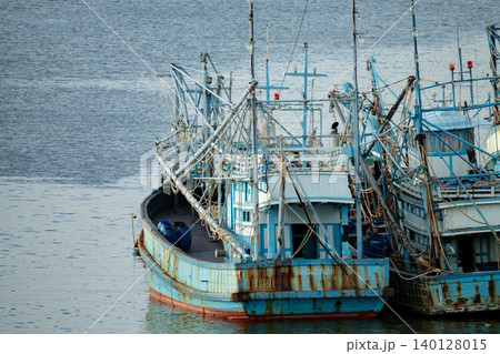 Old weathered blue fishing boats with rusty metal hulls moored at harbor dock with traditional rigging equipment for commercial fishing industry and maritime occupation coastal livelihood concept. Old weathered blue fishing boats with rusty metal hulls moored at harbor dock with traditional rigging equipment for commercial fishing industry and maritime occupation coastal livelihood concept. 140128015