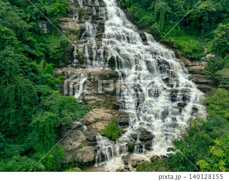 Aerial view of a waterfall in a lush tropical green forest in Doi Inthanon National Park, Chiang Mai, Thailand. This nature landscape showcases water sustainability and scenic travel destinations. Aerial view of a waterfall in a lush tropical green forest in Doi Inthanon National Park, Chiang Mai, Thailand. This nature landscape showcases water sustainability and scenic travel destinations. 140128155