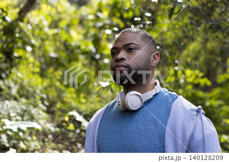 African American man wearing hoodie and headphones standing amid lush forest, copy space African American man wearing hoodie and headphones standing amid lush forest, copy space 140128209