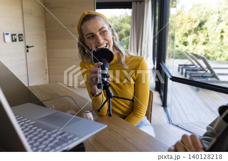 Woman speaking into studio microphone at home studio using laptop with cables wearing mustard top Woman speaking into studio microphone at home studio using laptop with cables wearing mustard top 140128218