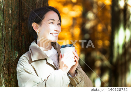 紅葉を楽しみながらホットドリンクを飲む女性 ライフスタイルイメージ 紅葉を楽しみながらホットドリンクを飲む女性 ライフスタイルイメージ 140128782