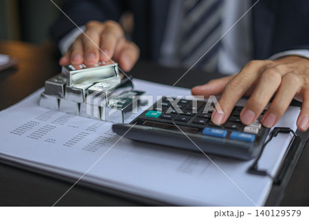 Silver Bullion Investment and Financial Analysis. Businessman Calculating Investment Returns with Silver Bars and Financial Documents. Silver Bullion Investment and Financial Analysis. Businessman Calculating Investment Returns with Silver Bars and Financial Documents. 140129579