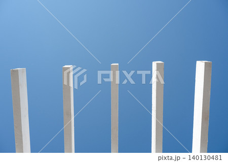 Abstract geometric pattern of white parallel sunshade poles with extensive negative space. Minimalist architectural background with white wooden beams and clear blue sky copy space. Abstract geometric pattern of white parallel sunshade poles with extensive negative space. Minimalist architectural background with white wooden beams and clear blue sky copy space. 140130481