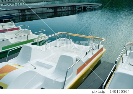 High angle view of white and yellow pedal boats parked at a modern pier on a calm lake, summer vacation and park recreation concept. 140130564