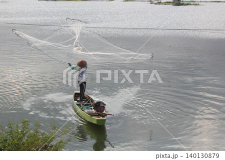 Traditional Fisherman Throwing a Cast Net from a Small Wooden Boat 140130879