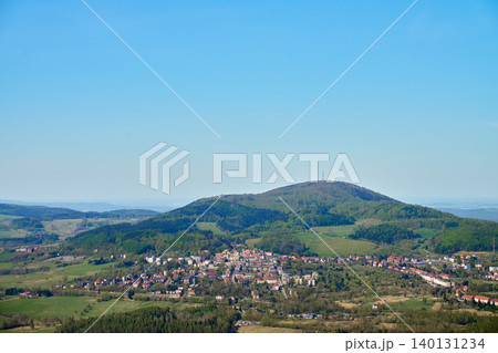 Small town sits below a green wooded hill with fields, rooftops and clear blue sky. Concept of countryside travel, rural landscape and tourism. Small town sits below a green wooded hill with fields, rooftops and clear blue sky. Concept of countryside travel, rural landscape and tourism. 140131234