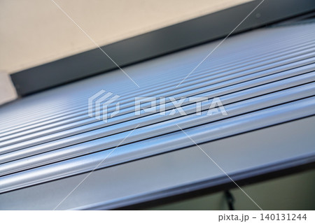 Closeup of a grey exterior roller shutter with horizontal metal slats installed above a modern house window. 140131244