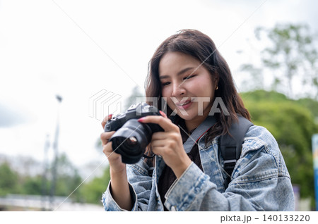 Close up of pretty asian woman holding and looking at camera checking photos while standing in park. 140133220