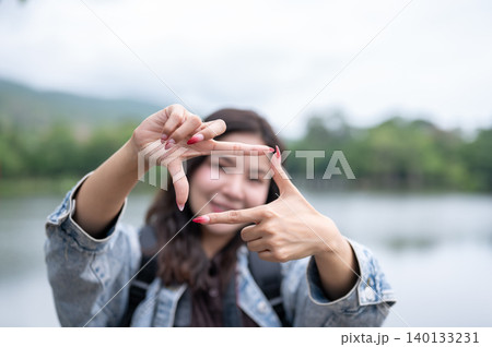Blurred asian woman doing hands framing gesture in front of a camera with reservoir lake in the back Blurred asian woman doing hands framing gesture in front of a camera with reservoir lake in the back 140133231