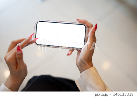 Close up of woman's long nails hands holding white screen phone as sitting indoors over tiles floor. 140133319