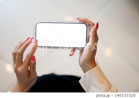 Close up of a woman's hands touching white screen smartphone while sitting indoors over tiles floor. Close up of a woman's hands touching white screen smartphone while sitting indoors over tiles floor. 140133320