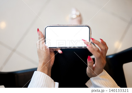 Close up of woman's long polished nails hand touching white screen smartphone while sitting indoors. Close up of woman's long polished nails hand touching white screen smartphone while sitting indoors. 140133321