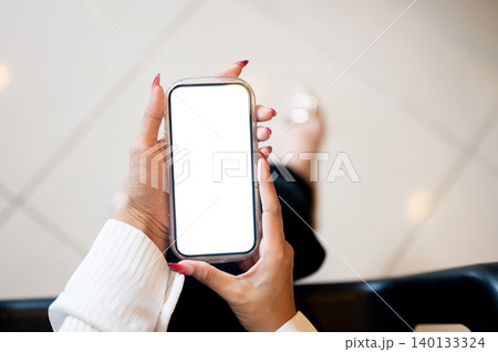 Close up of woman's long nail hands holding white screen phone while sitting indoors over tile floor Close up of woman's long nail hands holding white screen phone while sitting indoors over tile floor 140133324