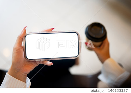 Close up of woman's long nails hand holding white screen phone in horizon and coffee sitting indoors Close up of woman's long nails hand holding white screen phone in horizon and coffee sitting indoors 140133327