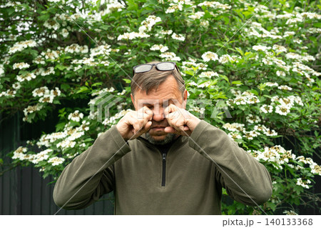 Middle aged man allergic suffering from seasonal allergy near blooming tree 140133368