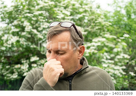 Middle aged man allergic suffering from seasonal allergy near blooming tree 140133369