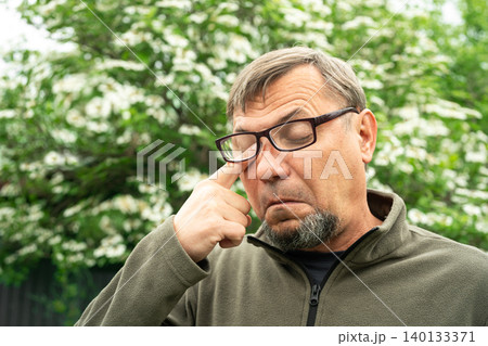 Senior man allergic suffering from seasonal allergy near blooming tree 140133371