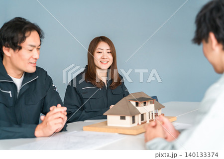 住宅模型を使って商談,説明,プレゼンする作業服姿の建設業,建築業の男女のビジネスマン 住宅模型を使って商談,説明,プレゼンする作業服姿の建設業,建築業の男女のビジネスマン 140133374