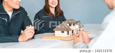 住宅模型を使って商談,説明,プレゼンする作業服姿の建設業,建築業の男女のビジネスマン 140133376