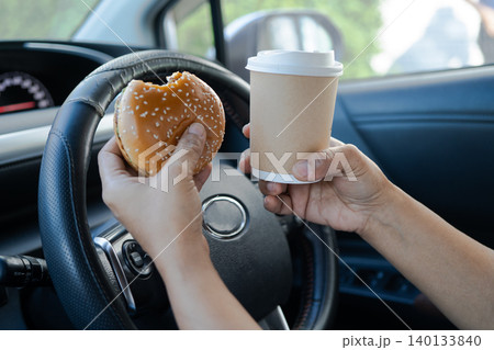 Asian lady holding ice coffee and bread bakery food in car dangerous and risk an accident. 140133840