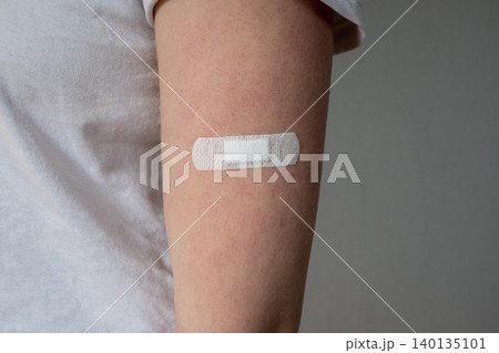 Young woman with medical adhesive plaster on the hand after vaccination. Fabric white bandage like first help for wound on the damage skin. Young woman with medical adhesive plaster on the hand after vaccination. Fabric white bandage like first help for wound on the damage skin. 140135101