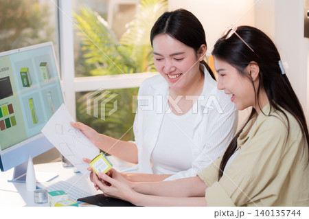 Two asian woman graphic designers analyzing product package prototype. Two asian woman graphic designers analyzing product package prototype. 140135744