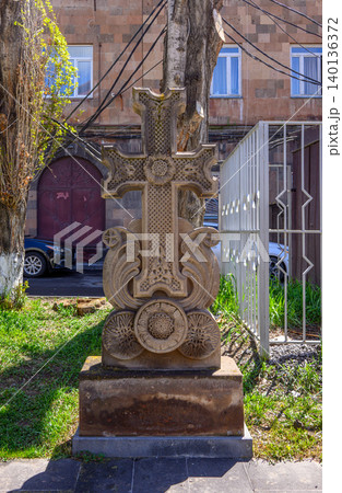 Carved stone cross in garden with metal fence and car behind 140136372