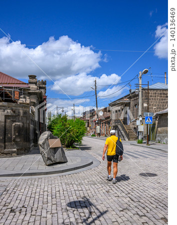 Person walks down cobblestone street under bright blue sky. Old stone buildings line the narrow path 140136469