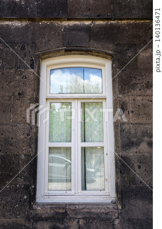 White window with glass panes, set in dark textured stone wall White window with glass panes, set in dark textured stone wall 140136471