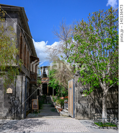 Narrow alleyway through historic stone buildings with trees and clear sky 140136473