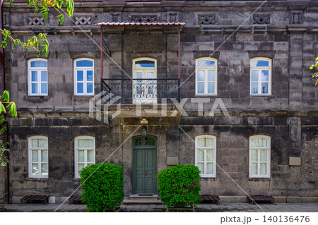 Old stone building with white-framed windows and green door. Decorative balcony with iron railing above entrance Old stone building with white-framed windows and green door. Decorative balcony with iron railing above entrance 140136476