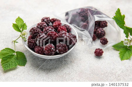 Frozen blackberries spilling from a bag into a bowl 140137532