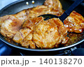 Juicy pork chops cooking in a frying pan with a savory glaze. A black spatula lifts one piece of tender meat. Close-up of home cooking process showing texture and sauce. High quality food photography. 140138270