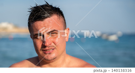 Wet caucasian man stands near the sea in Sharm El Sheikh Egypt with sunlight on his face and blurred beach background. Summer vacation and active lifestyle Wet caucasian man stands near the sea in Sharm El Sheikh Egypt with sunlight on his face and blurred beach background. Summer vacation and active lifestyle 140138316