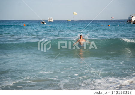 Caucasian man swims in sea waves near a beach in Sharm El Sheikh Egypt with boats and parasailing on the Red Sea horizon. Active vacation and resort lifestyle Caucasian man swims in sea waves near a beach in Sharm El Sheikh Egypt with boats and parasailing on the Red Sea horizon. Active vacation and resort lifestyle 140138318