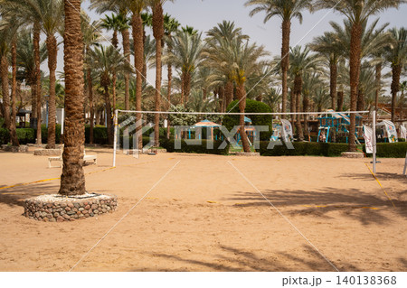 Empty beach volleyball court stands among palm trees at a tropical resort with sandy ground and recreation area in daylight. Travel and leisure Empty beach volleyball court stands among palm trees at a tropical resort with sandy ground and recreation area in daylight. Travel and leisure 140138368