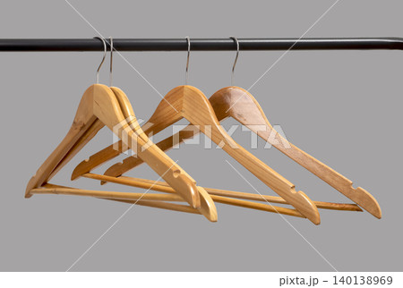 Wooden hangers hanging on black metal rack against neutral wall. Garment holders aligned on horizontal bar. Interior storage scene for wardrobe, retail, organization concept.. Wooden hangers hanging on black metal rack against neutral wall. Garment holders aligned on horizontal bar. Interior storage scene for wardrobe, retail, organization concept.. 140138969
