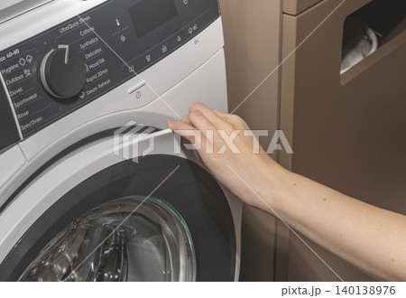 Woman touching washing machine control panel near door. Adult female adjusting program on front loading appliance. Domestic laundry concept for home, cleaning, lifestyle.. Woman touching washing machine control panel near door. Adult female adjusting program on front loading appliance. Domestic laundry concept for home, cleaning, lifestyle.. 140138976