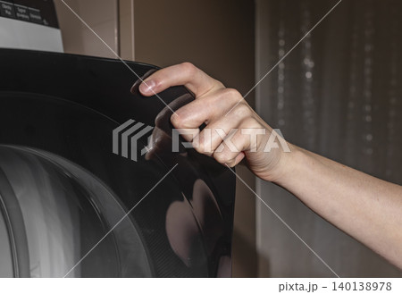 Woman touching black drying machine door glass. Adult female hand in laundry room. Domestic washing concept for home, household, lifestyle.. Woman touching black drying machine door glass. Adult female hand in laundry room. Domestic washing concept for home, household, lifestyle.. 140138978