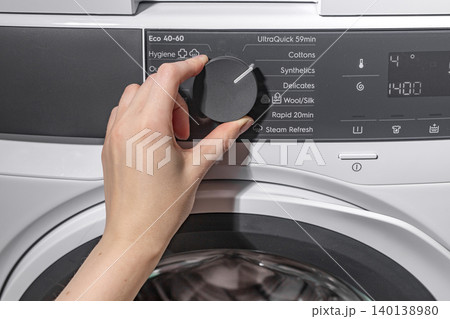 Woman setting washing machine cycle using control dial. Adult female adjusting front loading appliance program in laundry room. Domestic cleaning concept for home, household, lifestyle.. 140138980