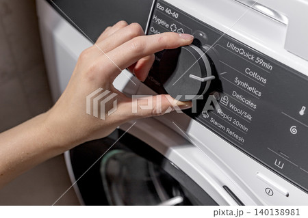 Woman selecting washing machine wash program on control panel. Adult female hand turning front loading appliance dial. Domestic laundry concept for home, cleaning, household lifestyle.. Woman selecting washing machine wash program on control panel. Adult female hand turning front loading appliance dial. Domestic laundry concept for home, cleaning, household lifestyle.. 140138981