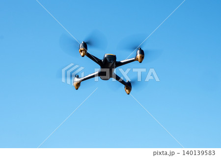 Black drone fllying in the blue sky. Innovative modern technology for work, game or entertainment. 140139583